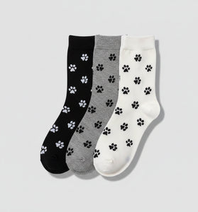 Three pairs of socks with paw prints in black, gray, and white on a woven surface.
