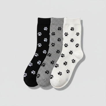 Three pairs of socks with paw prints in black, gray, and white on a woven surface.