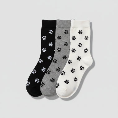 Three pairs of socks with paw prints in black, gray, and white on a woven surface.