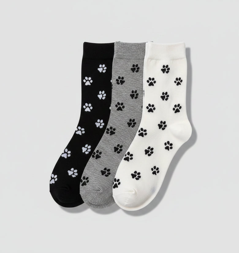 Three pairs of socks with paw prints in black, gray, and white on a woven surface.