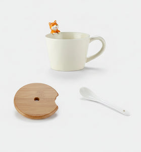 White mug with a small fox figure, wooden coaster, and white spoon on a white background