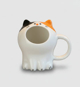 Cat-shaped mug on a wooden table with pastries in the background