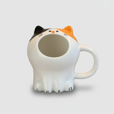 Cat-shaped mug on a wooden table with pastries in the background