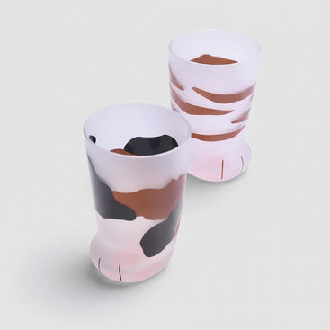 Two ceramic cups with animal print design on a white surface with coffee beans and a spoon.