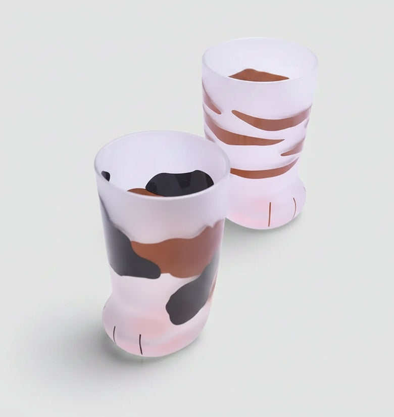Two ceramic cups with animal print design on a white surface with coffee beans and a spoon.