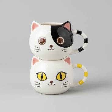 Two stacked ceramic cat-face mugs on a light gray background. The top mug has a black-and-white cat face with pink ears and a black-and-white striped handle.