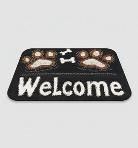 Black doormat with paw prints and 'Welcome' text on a wooden floor, next to a pair of slippers.