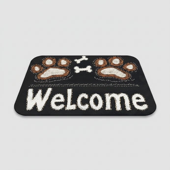 Black doormat with paw prints and 'Welcome' text on a wooden floor, next to a pair of slippers.