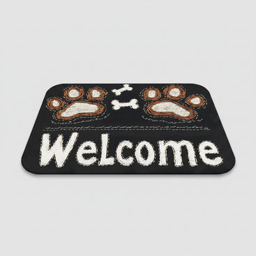 Black doormat with paw prints and 'Welcome' text on a wooden floor, next to a pair of slippers.