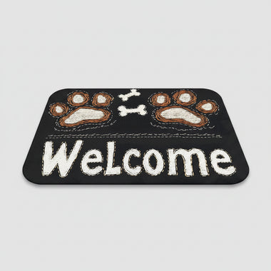 Black doormat with paw prints and 'Welcome' text on a wooden floor, next to a pair of slippers.