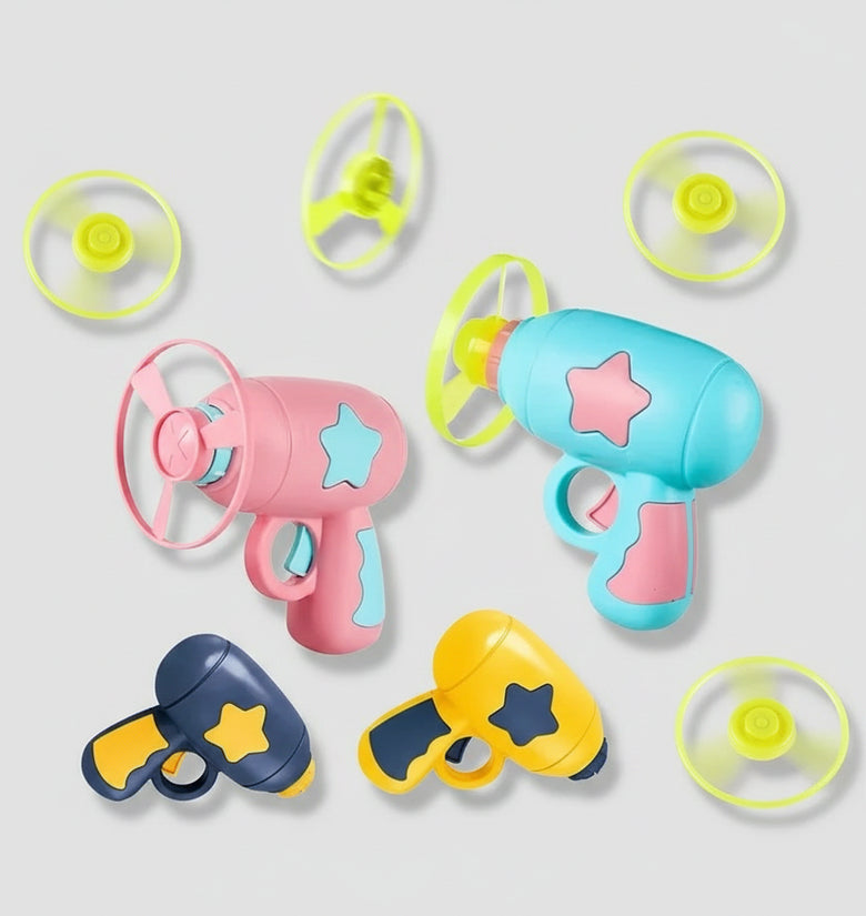 A set of colorful toy toy blasters and propeller attachments on a light gray background. The set includes three main blasters in pink, light blue, and yellow, each decorated with star-shaped cutouts, along with four separate propeller parts in neon yellow-green.