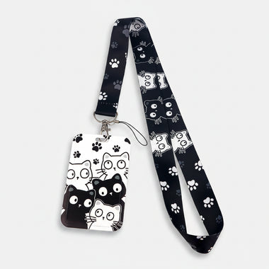 A black and white cat-themed lanyard with a matching ID badge holder. The fabric strap and badge are decorated with cartoon cat faces, paw prints, and spider webs in black and white.