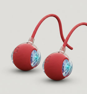 Red ball with a rope and light-up feature for cats, 2-pack, on a wooden floor with a cat in the background.