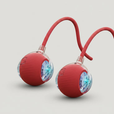 Red ball with a rope and light-up feature for cats, 2-pack, on a wooden floor with a cat in the background.