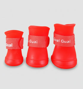 Three red pet boots with 'Guai Guai' branding on a wooden surface