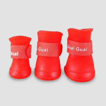 Three red pet boots with 'Guai Guai' branding on a wooden surface