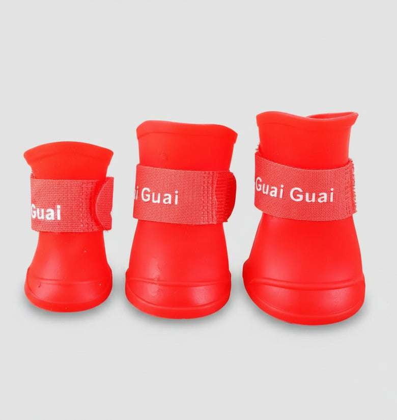 Three red pet boots with 'Guai Guai' branding on a wooden surface