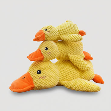 Three stacked yellow plush duck toys with orange beaks and black eyes, photographed on a light gray background.